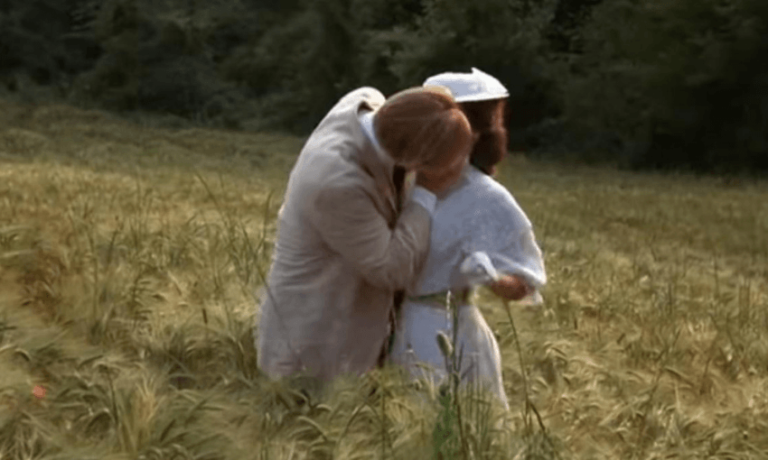 A man and a woman in period clothes, kissing in a poppy field.