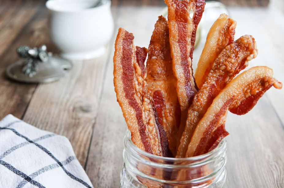 Side-by-side images of bacon slices being dehydrated in an oven and a dehydrator.